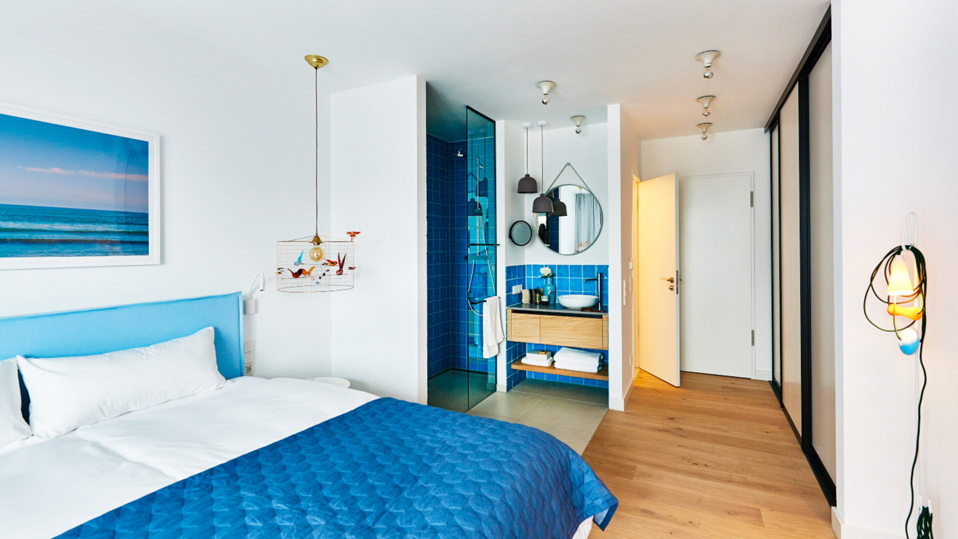 Blau eingerichtetes Doppelzimmer im Hotel New Wave auf Norderney mit Blick auf das offene Badezimmer und das Doppelbett.